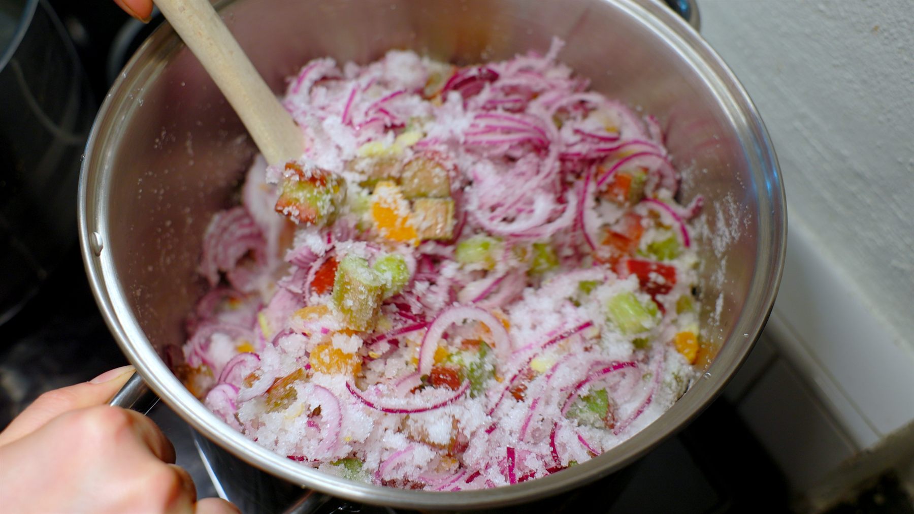 Närbild på rabarber, rödlök och socker i kastrullen innan chutneyn kokat ihop.
